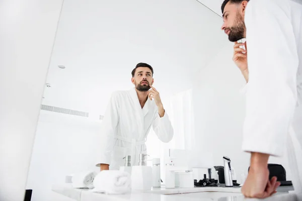 Hombre atento inclinándose al espejo y tocándose la cara — Foto de Stock