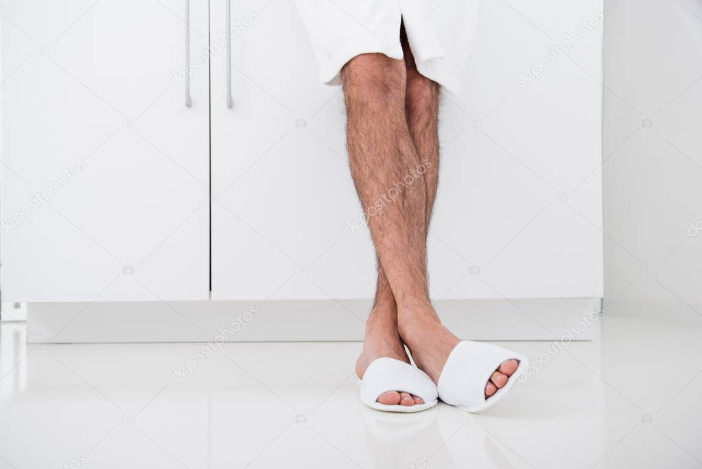 Close up of hairy male legs and white slippers on the feet