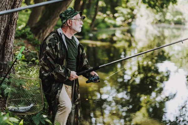 Professional aged fisherman holding a rod on the riverbank — Stock Photo, Image