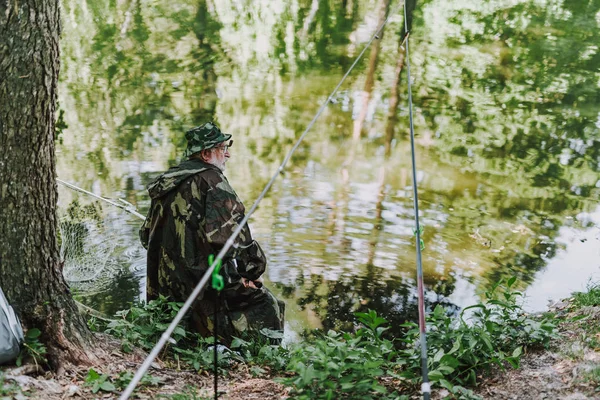 Rear view of an aged angler sitting on the river bank — Stock Photo, Image