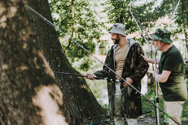 Positive bearded man fishing with his aged father — Stock Photo, Image