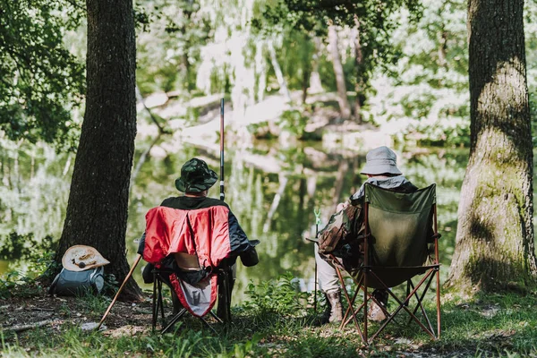 Rear view of men enjoying fishing on the river bank — Stock Photo, Image