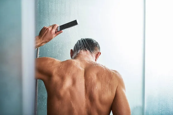 Joven hombre usando la cabeza de la ducha de mano mientras se lava en el baño —  Fotos de Stock