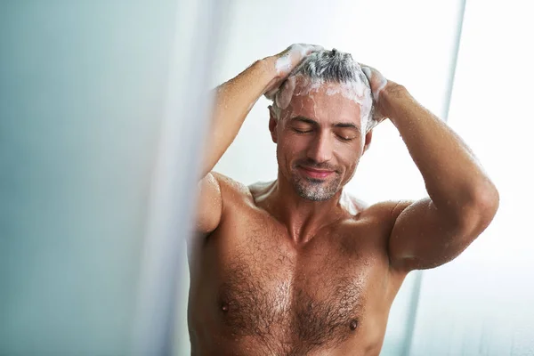 Pohledný mladý muž mytí vlasů při osprchování doma — Stock fotografie