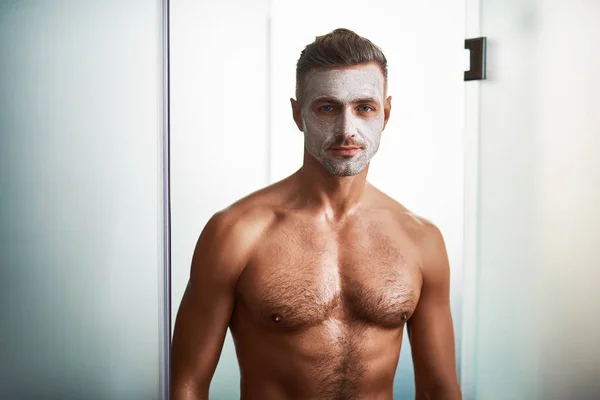 Beau jeune homme avec masque purificateur facial debout dans la porte de la douche — Photo