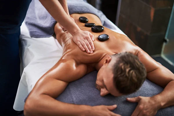 Massagista profissional massageando o corpo do cliente enquanto ele deitado na mesa de massagem — Fotografia de Stock