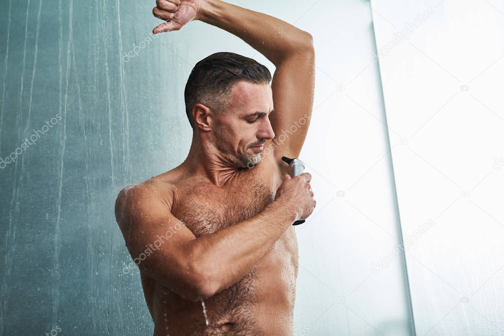 Handsome young man shaving armpit while taking shower