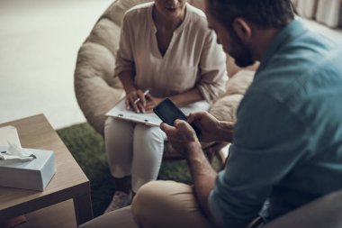 Akıllı telefon ve yakın oturan psikoterapist tutan adam