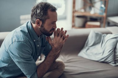 Ciddi orta yaşlı adam kanepede oturan ve düşünceli uzak ellerini yüzüne yakın yaparken seyir sakallı