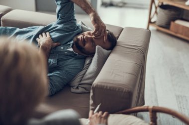 Kanepede oturan ve alnına dokunmak gülümseyen adam