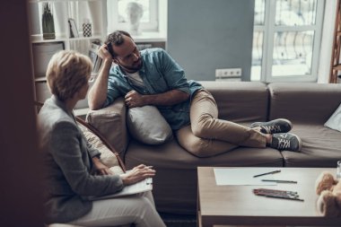 Adam kanepede oturan ve uzağa arıyorsunuz tam uzunlukta