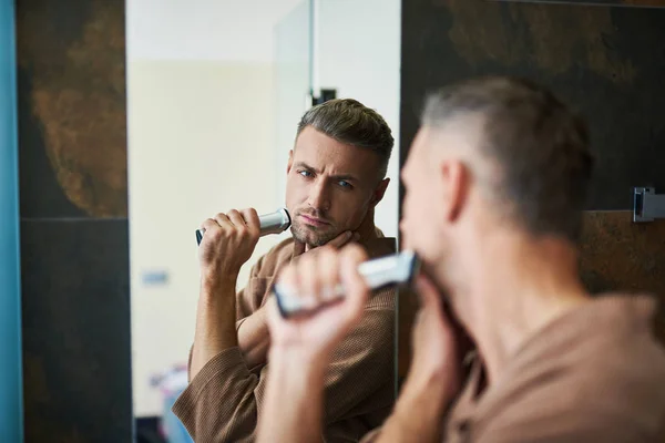 Atractivo hombre serio mirando en el espejo y afeitándose — Foto de Stock