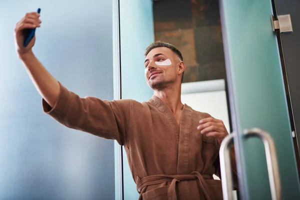 Hombre guapo con parches bajo los ojos haciendo selfie en el baño — Foto de Stock