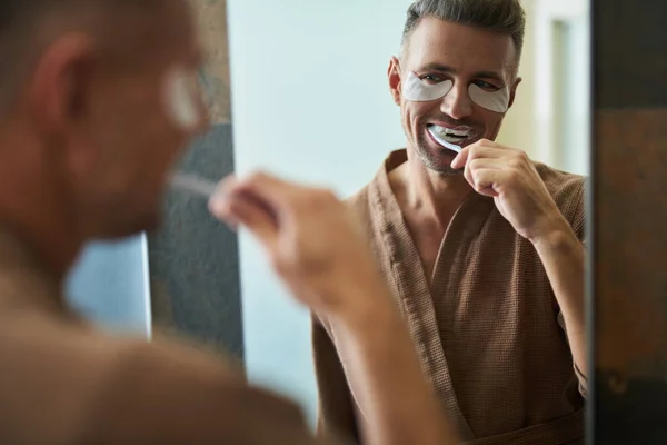 Bonito jovem com manchas sob os olhos escovando dentes — Fotografia de Stock