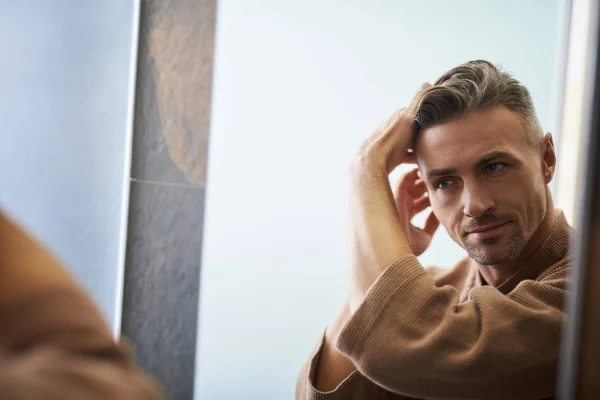 Joven guapo mirándose en el espejo en el baño — Foto de Stock