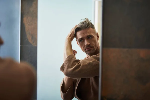Красивый молодой человек смотрит в зеркало в ванной комнате — стоковое фото