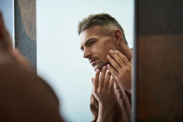 Hombre guapo sin afeitar mirando en el espejo en el baño en casa — Foto de Stock