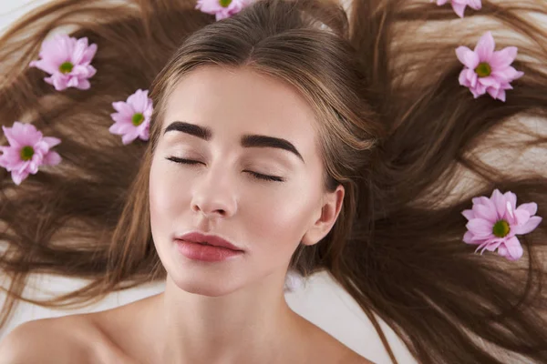 Relaxado jovem senhora com flores em seu cabelo deitado no fundo branco — Fotografia de Stock