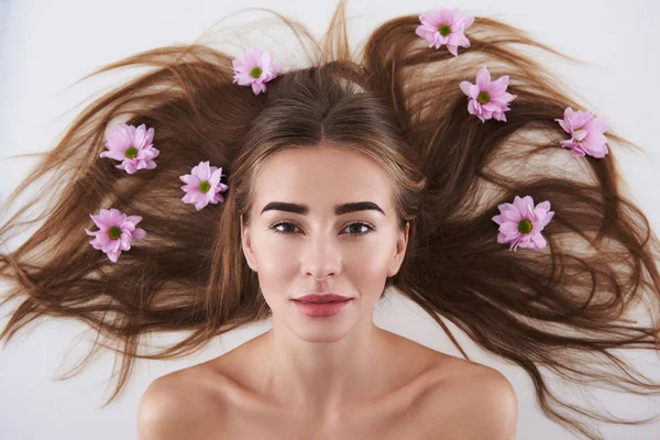 Aantrekkelijke jonge dame met bloemen in haar haar liggend op witte achtergrond — Stockfoto