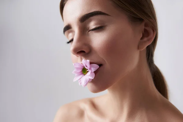 Ul junge Dame mit perfekter Haut hält rosa Blume im Mund — Stockfoto