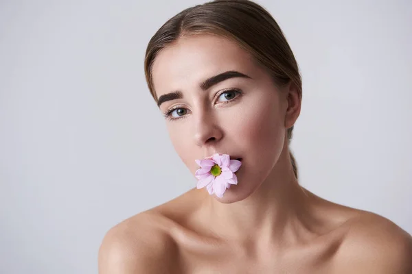 Mooie jonge dame met naakte schouders houden van roze bloem in mond — Stockfoto