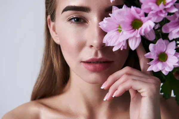 Jovem atraente cobrindo olho com belas flores rosa — Fotografia de Stock