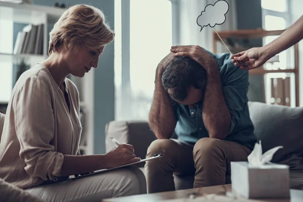 Hombre deprimido escondiendo su cara y psicoterapeuta haciendo notas — Foto de Stock