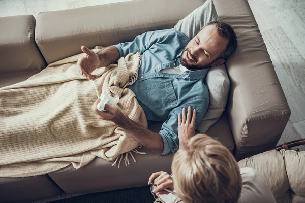 Эмоциональный человек лежит под одеялом и разговаривает с психотерапевтом — стоковое фото
