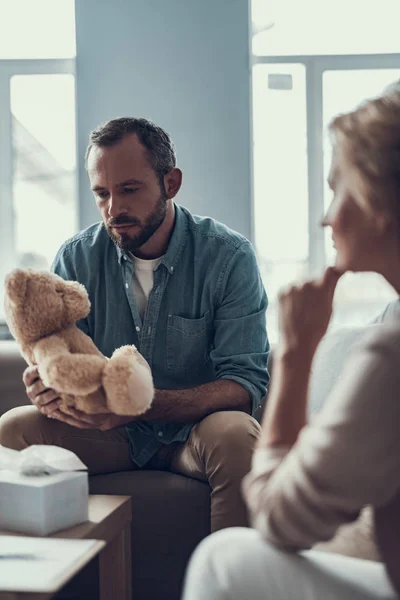 Cintura hacia arriba del hombre barbudo mirando pensativamente al oso de peluche — Foto de Stock