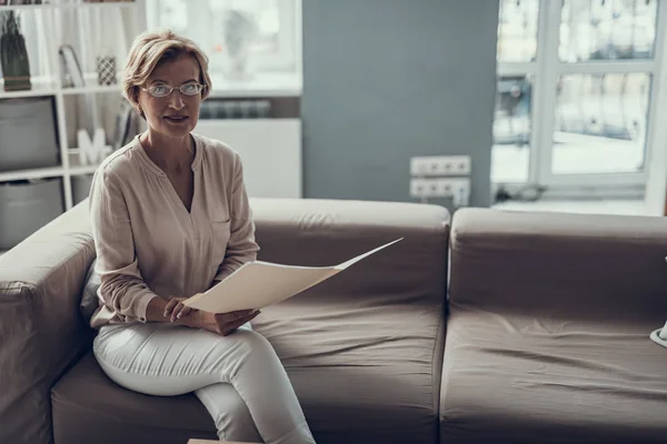 Спокойная женщина средних лет сидит с бумажной папкой на диване — стоковое фото
