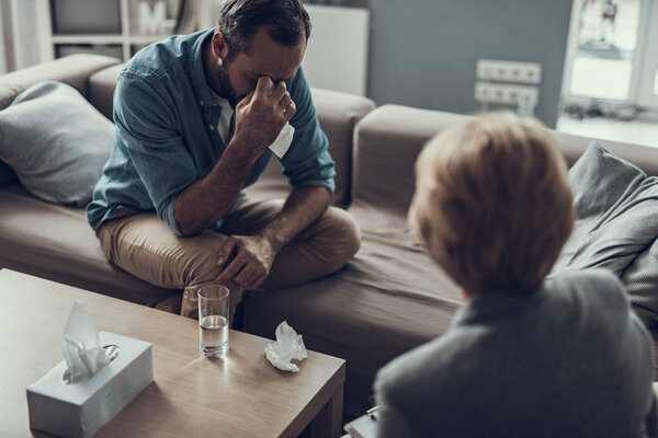 Sad man crying while sitting with his psychologist