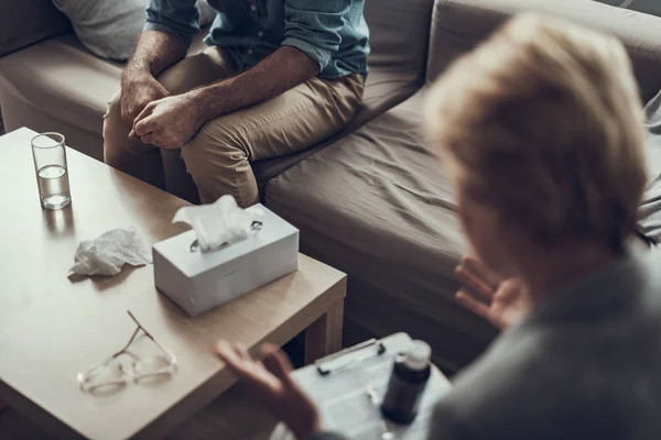 Mann sitzt auf dem Sofa und Frau gestikuliert vor ihm — Stockfoto