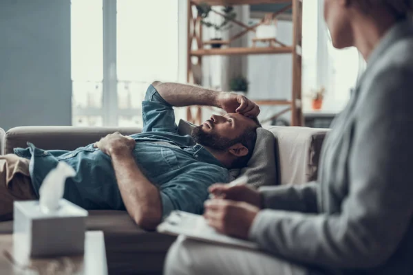 Nachdenklicher Mann blickt auf, während er auf dem Sofa liegt — Stockfoto