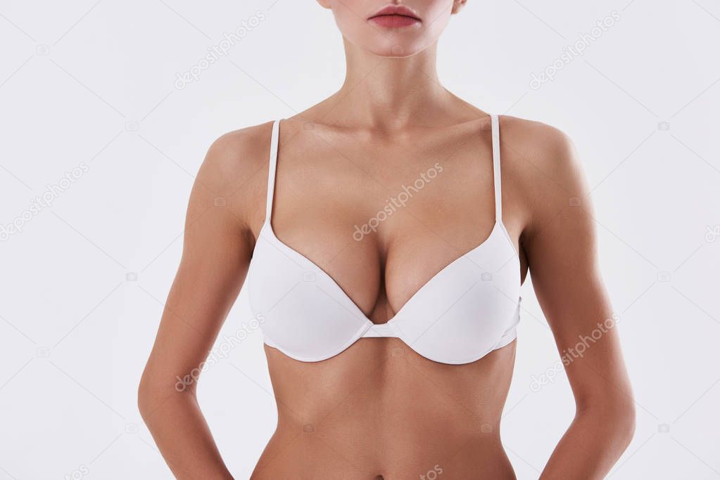 Attractive lady with beautiful breast in bra standing against white background
