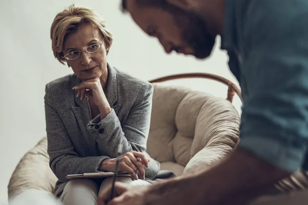 Calm psychotherapist watching her client drawing at the session