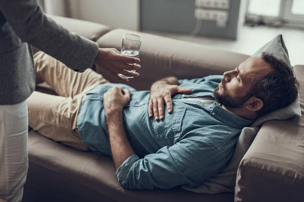 Trieste man liggend op de Bank en behulpzaam persoon bieden hem water — Stockfoto