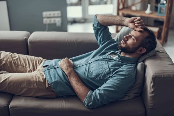 Взрослый мужчина лежит на диване и закрывает глаза, находясь дома — стоковое фото