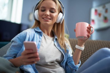 Müzik dinleme ve cep telefonu kullanarak sıcak içecek neşeli güzel kız