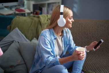 Sıcak bir içecek müzik dinleme genç kadınla büyüleyici ve cep telefonu kullanarak