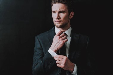 Koyu takım elbise ayakta siyah duvara karşı ciddi adam