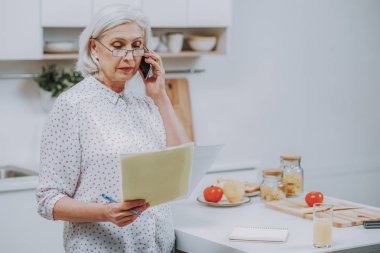 Üst düzey kadın kapalı yemek yaparken telefonla konuşuyor