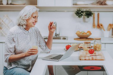 Mutlu olgun kadın evde pişirme sırasında dizüstü izliyor