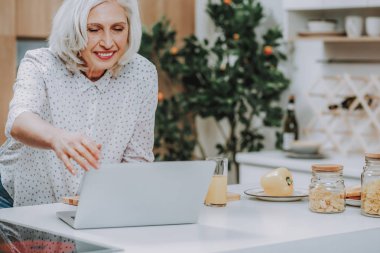 Neşeli olgun kadın yemek hazırlama laptop kullanıyor