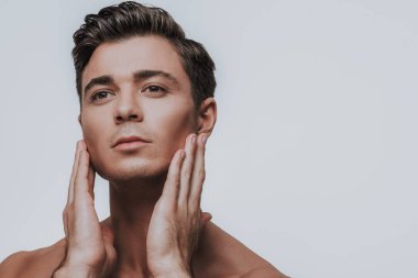Sakin yakışıklı genç adam yanakları dokunmadan eller ile sakin ve düşünceli duran gri arka planı arıyorum