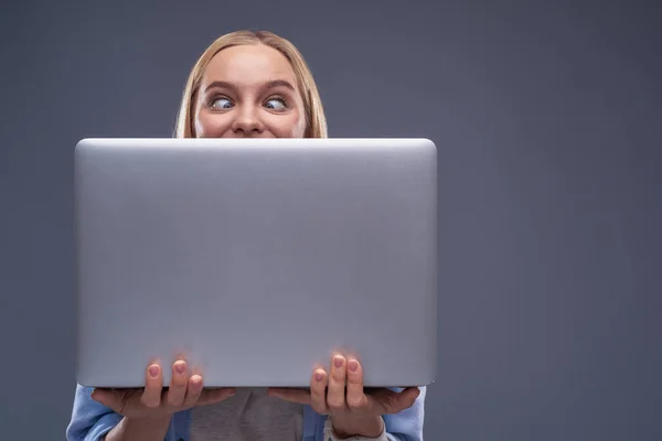 Divertente giovane signora che si nasconde dietro il computer portatile argento — Foto Stock