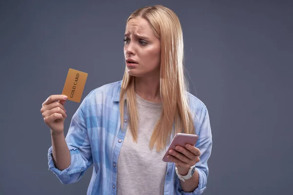 Sconvolto giovane signora con il cellulare guardando la carta d'oro — Foto Stock