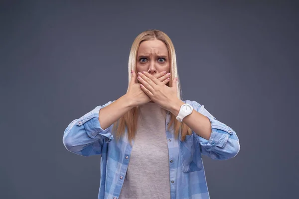 Giovane donna irritata in camicia blu che copre la bocca con le mani — Foto Stock