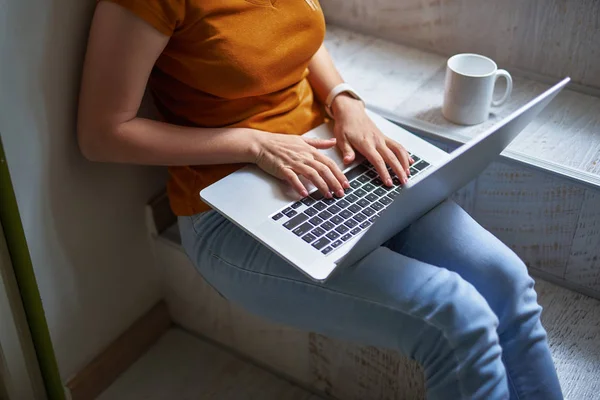 Young lady in orange shirt working on laptop at home — Stock Photo, Image