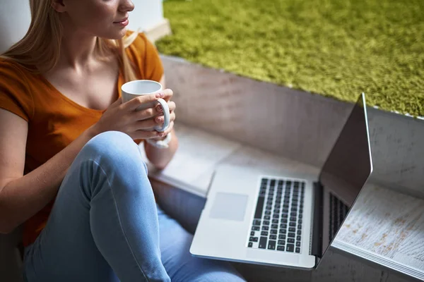 Vacker ung dam med varm dryck med laptop hemma — Stockfoto