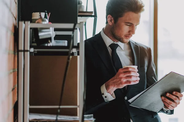 Ήρεμος άνθρωπος σε σκούρο κοστούμι βλέπουν τις σημειώσεις του, πίνοντας τον καφέ — Φωτογραφία Αρχείου